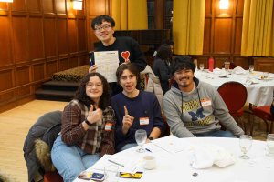 Students sitting at table smiling and holding up a bingo sheet.
