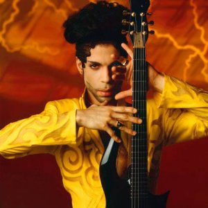 Photo of Prince, wearing an ornate yellow jacket and holding a guitar in front of n orange background