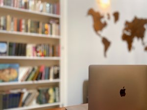 laptop on a desk with a book shelf and wall map in the background