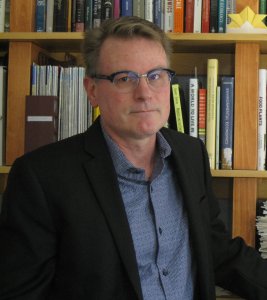Bill Currie, a white man standing in front of book shelf