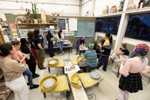 Students gather around a pottery wheel to watch a demo in the Stamps Ceramics studio.