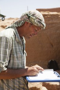 Geoff Emberling writing on a clipboard at an excavation site.