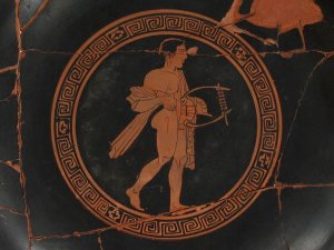 Close-up view of the inside of a black and red kylix, showing a nude male figure holding a lyre and encircled by a decorative border.