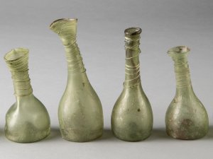 A line of four green glass bottles with narrow spouts that lean to the side.