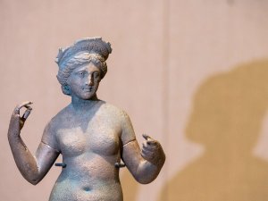 Nude statue of the goddess Aphrodite, standing with her arms upraised and wearing a diadem.