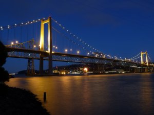 Photograph, illuminated bridge at night over water.
