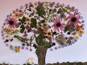Artwork featuring a tree crafted from nature parts such as leaves and flowers, as well as craft gems