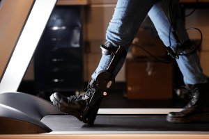 A close up of a person wearing an ankle exoskeleton while walking on a treadmill.