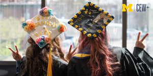 2 graduates with backs to the camera wearing decorated graduation caps and giving the peace sign