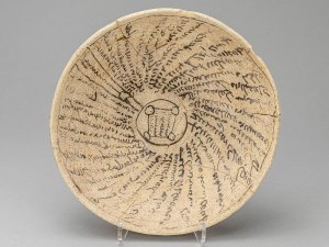 Incantation bowl made of tan clay with black inscriptions radiating from the center.