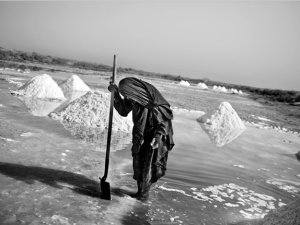 A person with a shovel stands near piles of harvested salt.