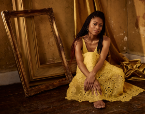 Pianist Isata Kanneh-Mason sitting on the floor in a yellow dress.