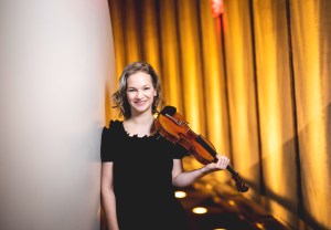 Violinist Hilary Hahn posing smiling with her violin.