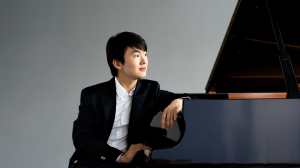 Pianist Seong-Jin Cho seated at a piano smiling.
