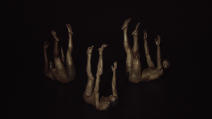 Three dancers from TRIBE, seemingly falling surrounded by darkness with their arms and legs extended into the air.