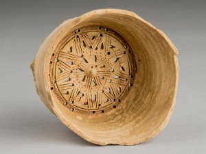 Clay water filter with a star-shaped geometric pattern and pierced holes at its base.