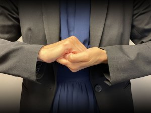 Light-skinned woman with interlocking hands in front of her chest, the American Sign Language sign for collaborate.
