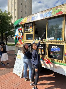 Two students stand at delivery window of Kona Ice Truck.