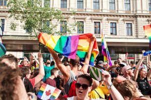 A large crowd of people stand with pride flags outside on a sunny day