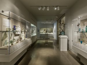 View of the Kelsey Museum’s first floor galleries. In the foreground are vitrines with colorfiul glass vessels; in the background are cases with various objects from Graeco-Roman Egypt.
