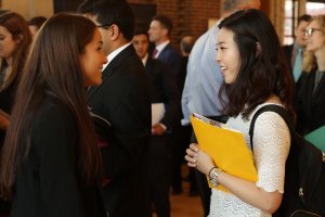 Two young women conversing at a professional event, one holding a yellow folder