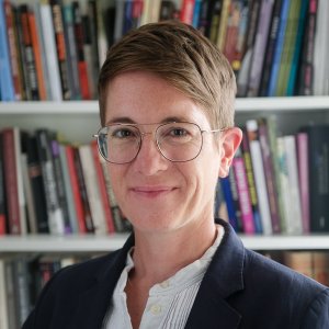Smiling woman with short brown hair with a bookshelf background.