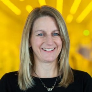 Headshot of Allison Steiner (white woman with blonde hair) on a yellow background.