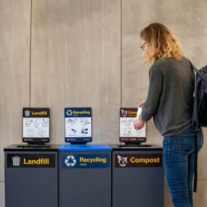 A woman throws an item into a recycle bin.