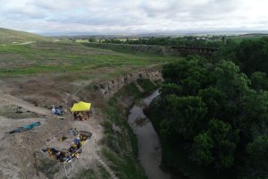 Archaeological field site with working crew situated next to a deep ravine with a creek at the bottom
