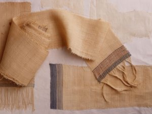 Several tan woven textiles with blue and red stripes and fringe at their ends.