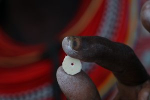 Thumb and index finger holding a round ostrich eggshell bead with hole in the middle