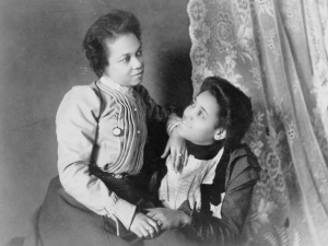 Two African American women, three-quarter length portrait, seated, facing each other