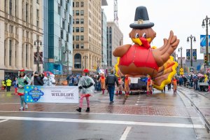 Woodward Avenue shot of volunteers pulling the turkey balloon, surrounded by parade crowds lining the sidewalk.