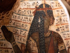 Close-up of the coffin of Djehutmose, showing a side view of the Egyptian goddess Amentet wearing a braided black wig and a red garment, surrounded by hieroglyphs.