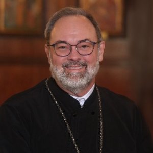 Image shows the guest speaker of the event, Father Barnabas Powell. He is shown smiling, wearing black robes, a gold chain, and glasses. Image shows the guest speaker of the event, Father Barnabas Powell. He is shown smiling, wearing black robes, a gold chain, and glasses.