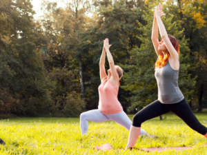 Two people doing a yoga pose outside with bent legs and their arms above their heads