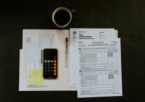 Image of a calculator, pen, and tax formers sitting on top of a budget sheet, next to a cup of coffee.