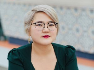 Headshot of Angela Chen (white blond short hair, glasses, red lip).