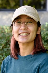 Photo of a girl with brown hair and glasses wearing a teal shirt and a tan New York hat smiles at the camera Photo of a girl with brown hair and glasses wearing a teal shirt and a tan New York hat smiles at the camera