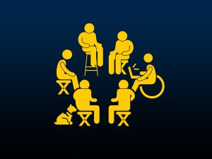 6 people sit in a circle on various chairs and assistive devices. 1 person has a service dog and another holds a laptop. 6 people sit in a circle on various chairs and assistive devices. 1 person has a service dog and another holds a laptop.