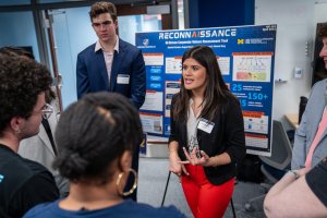 Students present research in front of poster board