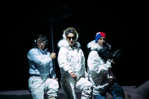 3 people dressed in snow gear on dark stage
