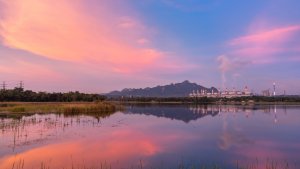 scenic sunset over lake with mountains, power plant in background