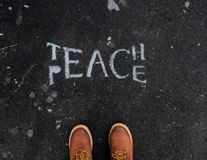 brown boots stand on black asphalt looking at a chalking that reads "Teach Peace" brown boots stand on black asphalt looking at a chalking that reads "Teach Peace"