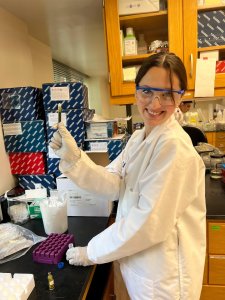 A woman in a lab coat and protective eyewear holds up a test tube in a laboratory A woman in a lab coat and protective eyewear holds up a test tube in a laboratory