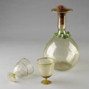 Three pieces of green glass from the Kelsey Museum’s collection: two small cups with short stems and a taller flask with a rounded belly and a narrow spout plugged by organic material.