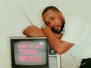 Cuee rests on a television displaying "This is my trans world" Cuee rests on a television displaying "This is my trans world"