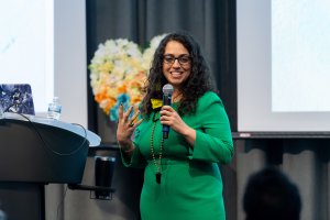 Rebecca Irby speaking by a podium with a paper crepe heart in the background Rebecca Irby speaking by a podium with a paper crepe heart in the background