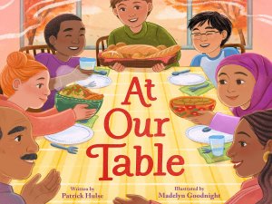 The cover of the picture book “At Our Table,” showing a multicultural group of adults and children sitting around a dining table holding bowls of food. The cover of the picture book “At Our Table,” showing a multicultural group of adults and children sitting around a dining table holding bowls of food.