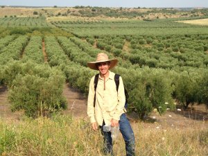 David Stone wearing a hat and standing in the tall grass in front of a green field of rows of bushes. David Stone wearing a hat and standing in the tall grass in front of a green field of rows of bushes.